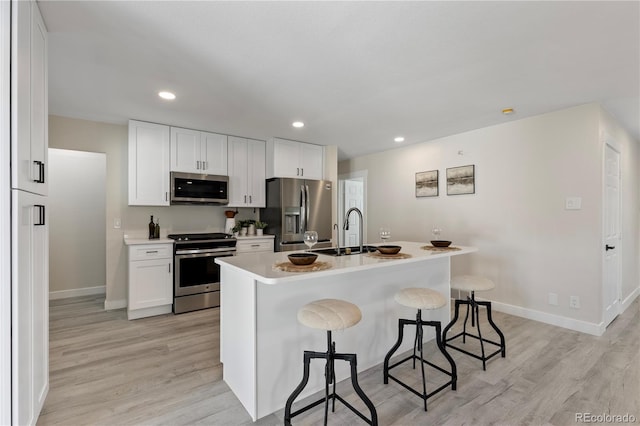 kitchen with a center island with sink, light countertops, appliances with stainless steel finishes, a sink, and a kitchen bar