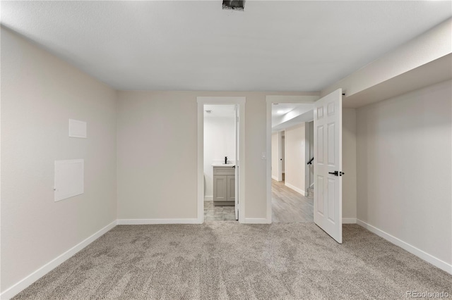 unfurnished bedroom featuring baseboards, ensuite bathroom, a sink, and light colored carpet