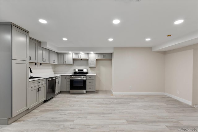 kitchen featuring gray cabinetry, a sink, light countertops, appliances with stainless steel finishes, and light wood finished floors