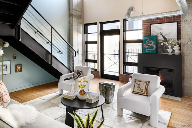 living area featuring wood finished floors, stairway, a glass covered fireplace, and a high ceiling