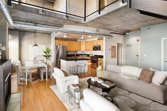 living room featuring light wood-type flooring, a towering ceiling, and visible vents