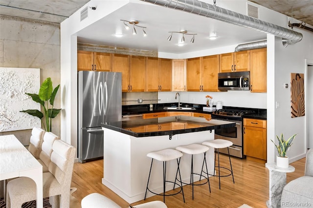 kitchen with appliances with stainless steel finishes, dark countertops, light wood-style floors, and a sink