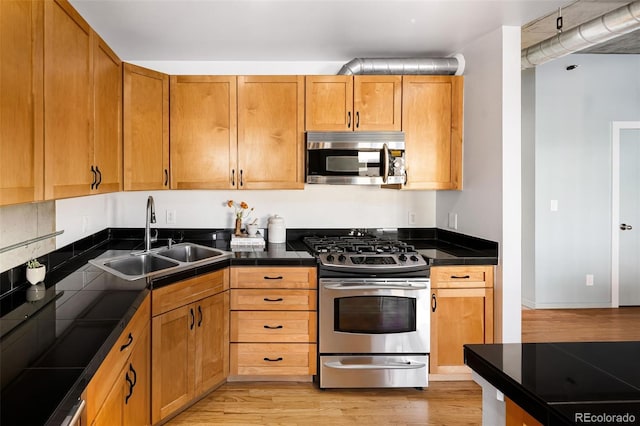 kitchen with appliances with stainless steel finishes, a sink, tile counters, and light wood-style floors