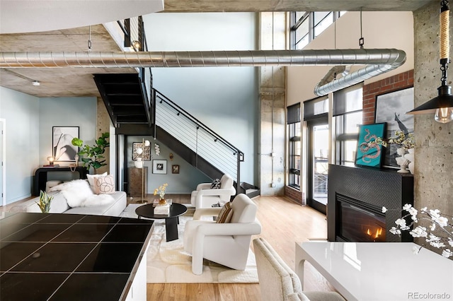 living room featuring stairs, a high ceiling, wood finished floors, and a glass covered fireplace