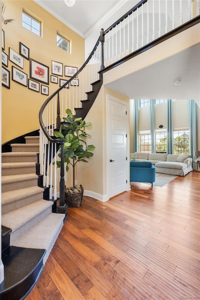 stairway with a high ceiling, baseboards, crown molding, and wood finished floors