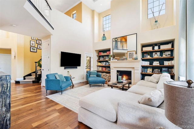 living area featuring built in features, a warm lit fireplace, stairway, and wood finished floors