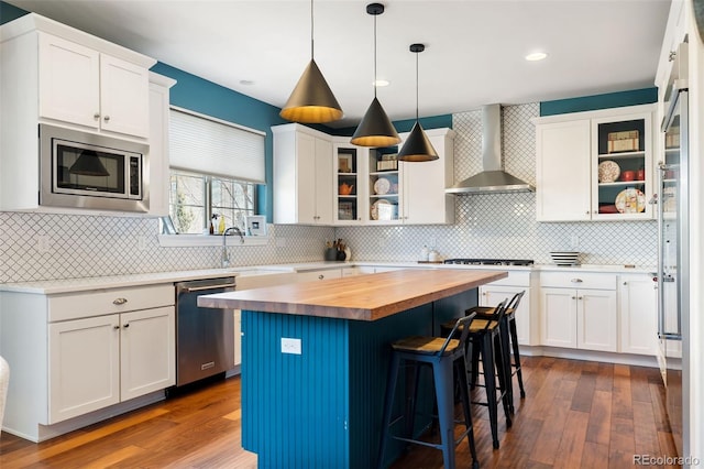 kitchen featuring butcher block counters, a sink, white cabinetry, appliances with stainless steel finishes, and wall chimney exhaust hood