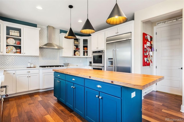 kitchen featuring appliances with stainless steel finishes, blue cabinetry, wood counters, and wall chimney exhaust hood