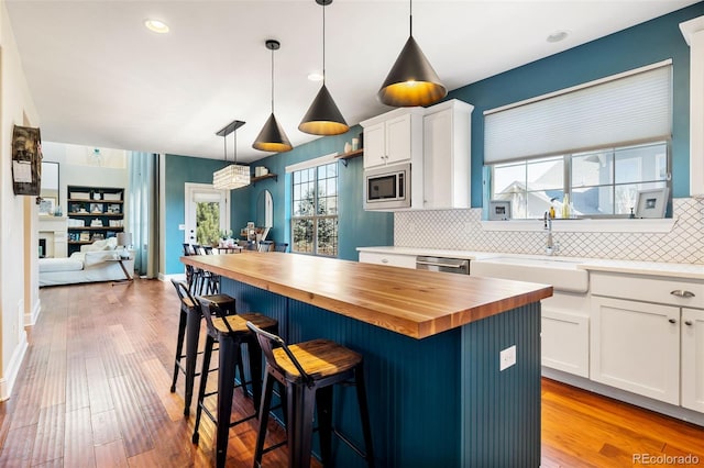 kitchen with white cabinets, butcher block countertops, stainless steel appliances, light wood-type flooring, and a sink