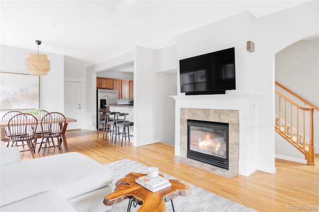 living room with arched walkways, light wood-style flooring, stairway, and a tile fireplace