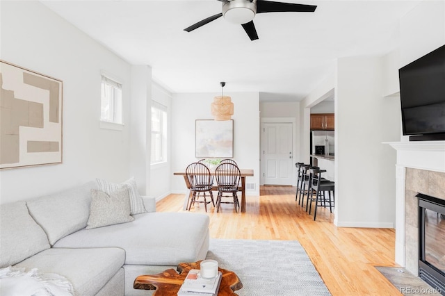 living room with a fireplace with flush hearth, baseboards, ceiling fan, and light wood-style flooring