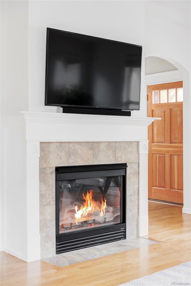 room details with a tiled fireplace, arched walkways, and wood finished floors