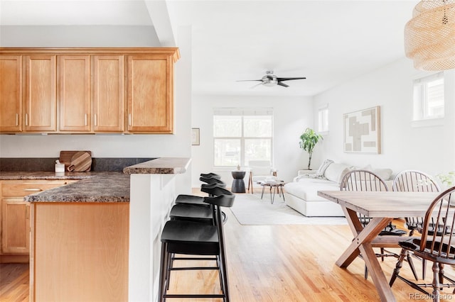 kitchen featuring dark countertops, light wood finished floors, a breakfast bar area, a ceiling fan, and open floor plan