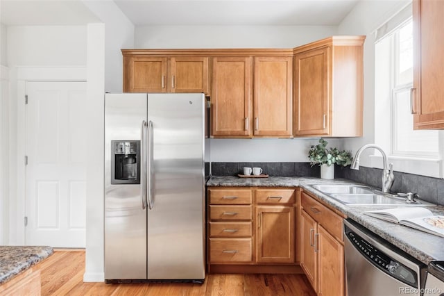 kitchen with a sink, light wood finished floors, appliances with stainless steel finishes, and a healthy amount of sunlight
