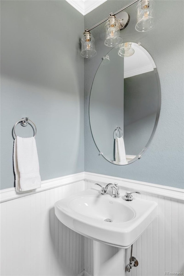 bathroom featuring a sink, ornamental molding, and wainscoting