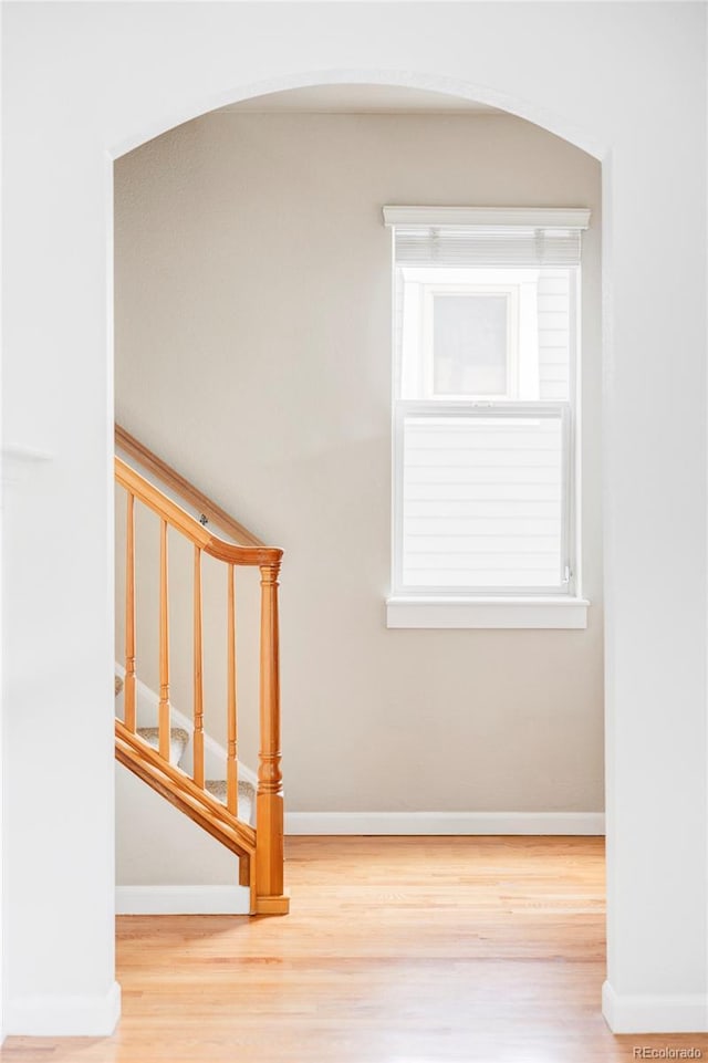 stairs featuring arched walkways, baseboards, and wood finished floors