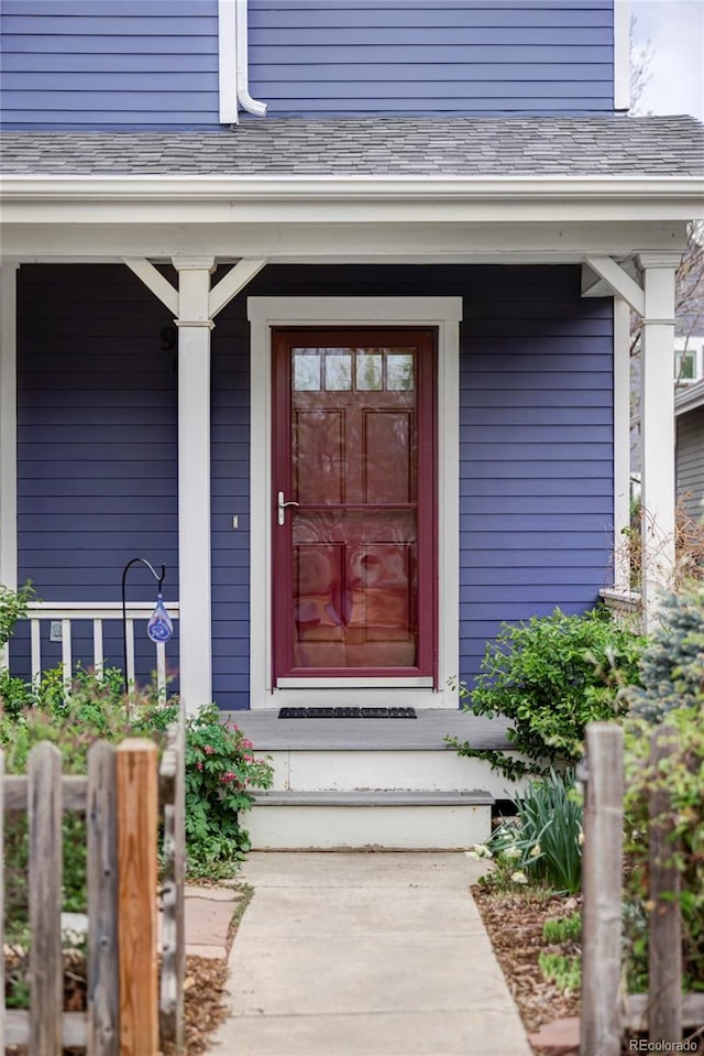 view of exterior entry with a porch and roof with shingles