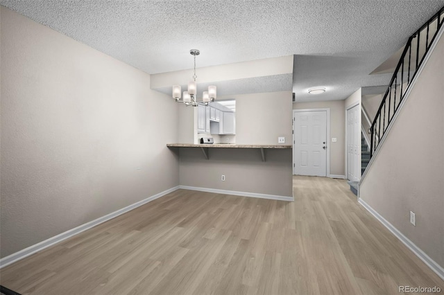 interior space with baseboards, light wood-type flooring, a textured ceiling, and a notable chandelier
