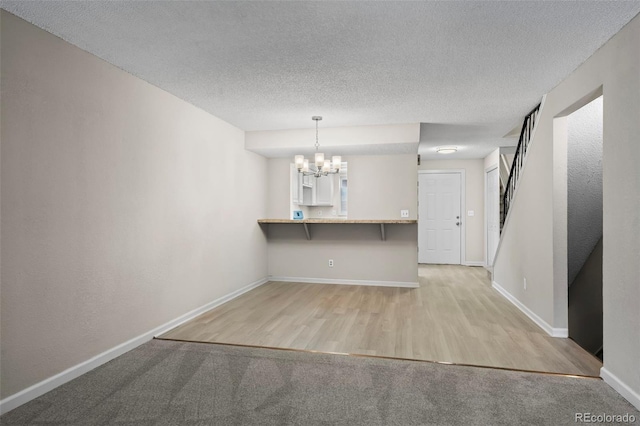 interior space featuring a textured ceiling, baseboards, a notable chandelier, light wood-style floors, and light carpet