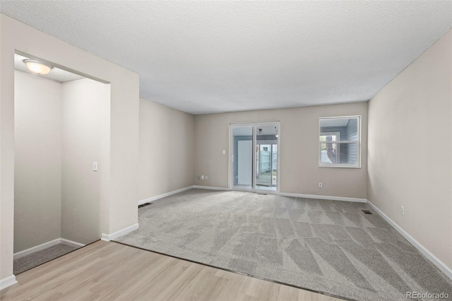 empty room featuring baseboards, carpet floors, a textured ceiling, and wood finished floors