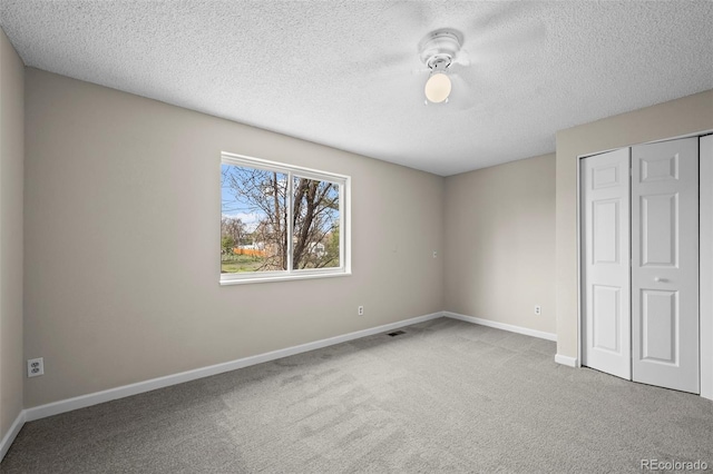 unfurnished bedroom featuring carpet flooring, a textured ceiling, baseboards, visible vents, and a closet