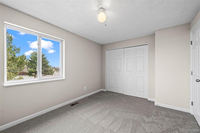 unfurnished bedroom featuring visible vents, a textured ceiling, carpet floors, and baseboards