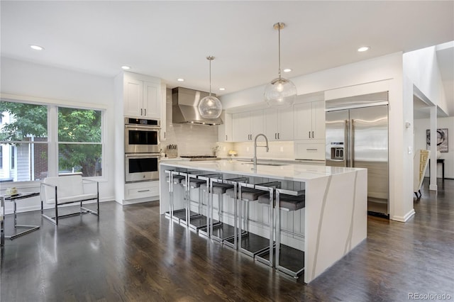 11389 E Maplewood Ave, Englewood, CO 80111 - kitchen with stainless steel appliances, wall chimney exhaust hood, backsplash, white cabinetry, and dark wood finished floors