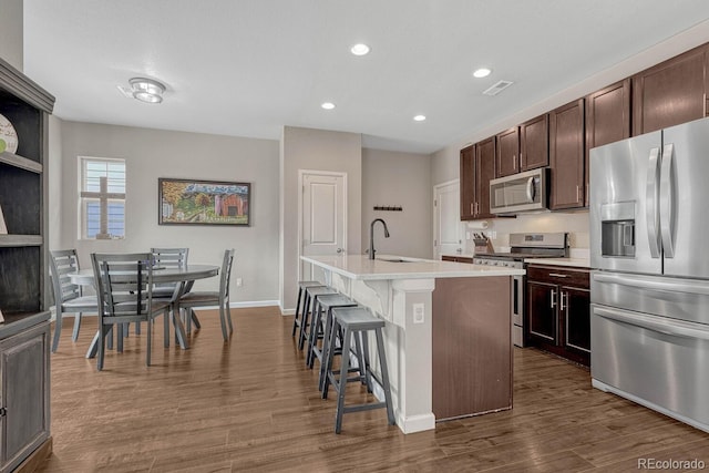 kitchen with a kitchen island with sink, sink, a breakfast bar area, dark hardwood / wood-style floors, and stainless steel appliances