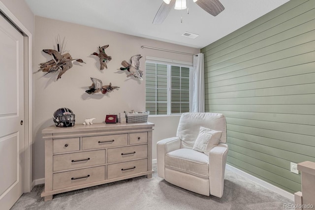 living area featuring wooden walls, ceiling fan, and light carpet