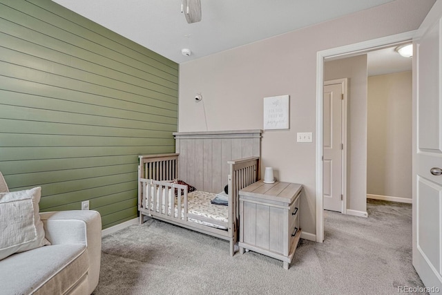 bedroom with ceiling fan, a crib, light carpet, and wooden walls