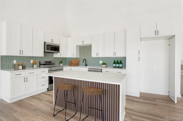 kitchen featuring sink, stainless steel appliances, light hardwood / wood-style floors, white cabinets, and a kitchen island