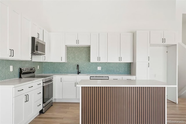 kitchen with a center island, appliances with stainless steel finishes, white cabinets, light hardwood / wood-style floors, and backsplash