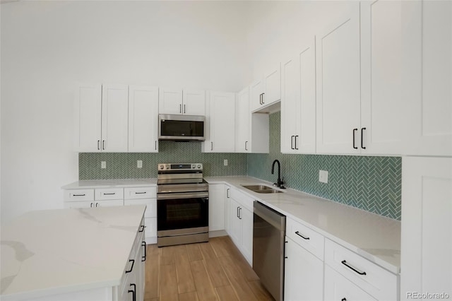 kitchen with light stone countertops, appliances with stainless steel finishes, sink, and white cabinets