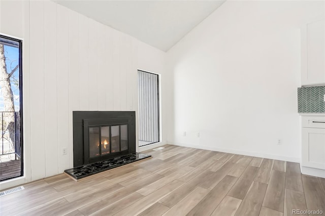 unfurnished living room with a tiled fireplace, vaulted ceiling, and light hardwood / wood-style flooring