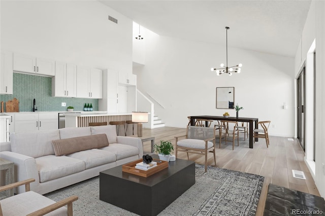 living room featuring an inviting chandelier, a towering ceiling, and light hardwood / wood-style floors