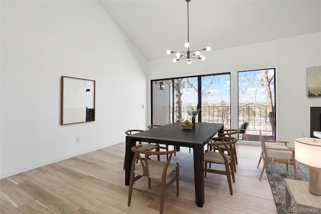 dining space with high vaulted ceiling, an inviting chandelier, and light hardwood / wood-style flooring