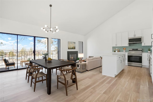 dining room featuring an inviting chandelier, high vaulted ceiling, and light wood-type flooring