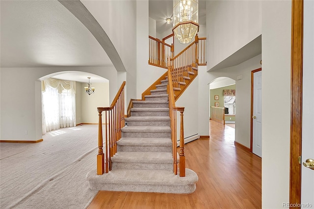 staircase featuring arched walkways, plenty of natural light, a chandelier, and baseboard heating
