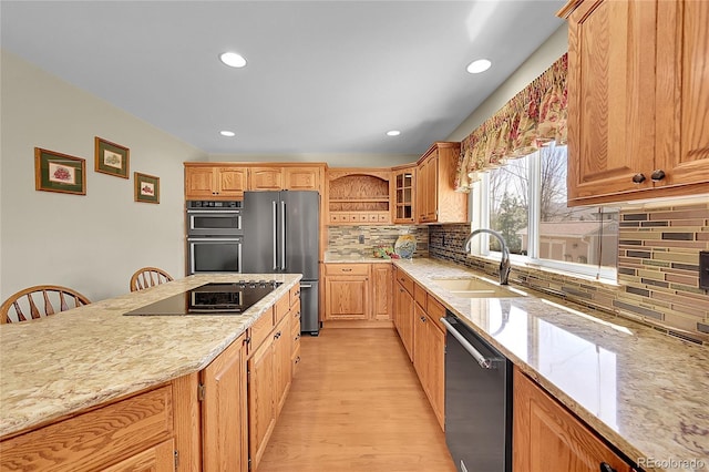 kitchen with appliances with stainless steel finishes, light stone counters, a sink, light wood finished floors, and decorative backsplash