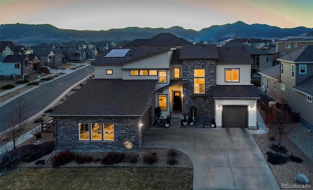 view of front facade featuring a mountain view, a garage, a residential view, stone siding, and driveway