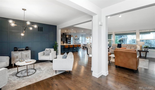 living room featuring dark wood-type flooring, an inviting chandelier, visible vents, and a decorative wall