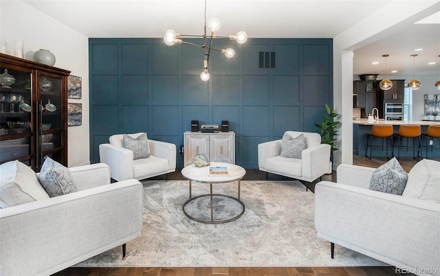 living room with an inviting chandelier, wood finished floors, visible vents, and a decorative wall