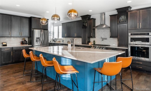 kitchen with stainless steel appliances, a sink, wall chimney range hood, and dark wood-style floors