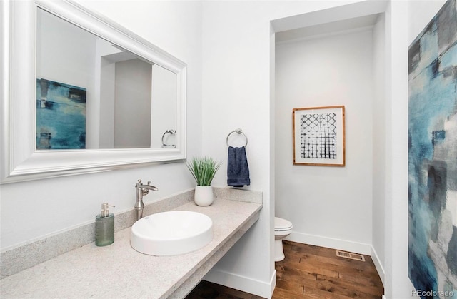 bathroom with visible vents, toilet, a sink, wood finished floors, and baseboards