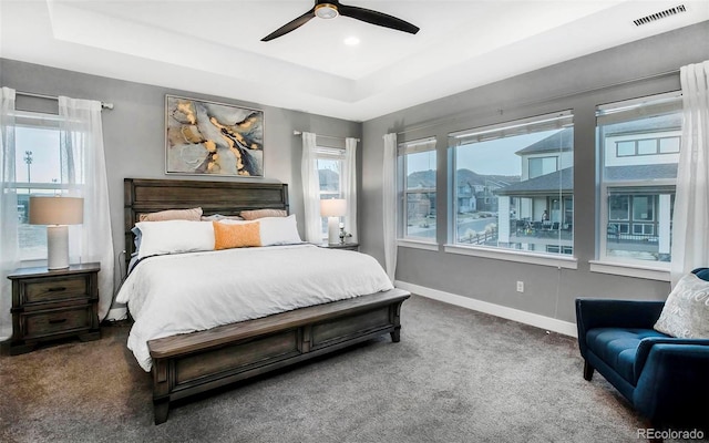 bedroom featuring a raised ceiling, visible vents, baseboards, and multiple windows