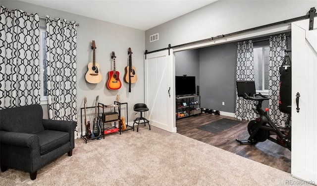 living area with a barn door, wood finished floors, visible vents, and baseboards