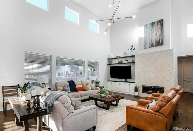 living room with a glass covered fireplace, a healthy amount of sunlight, an inviting chandelier, and wood finished floors