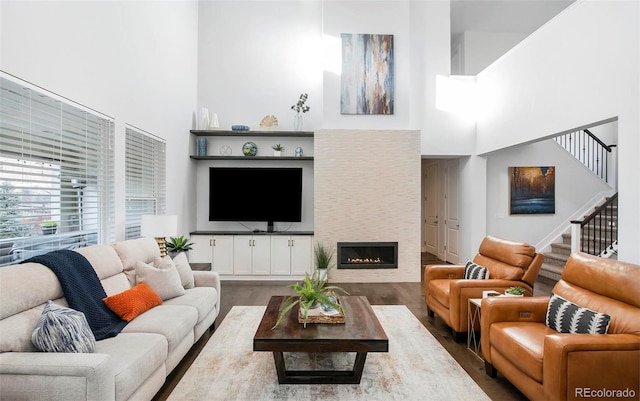 living room featuring a warm lit fireplace, dark wood-style flooring, a high ceiling, and stairs