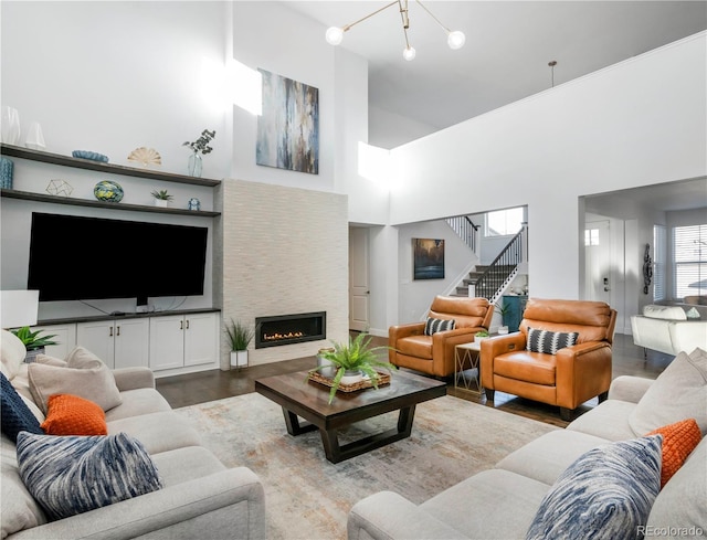 living area featuring a warm lit fireplace, a high ceiling, stairway, and wood finished floors