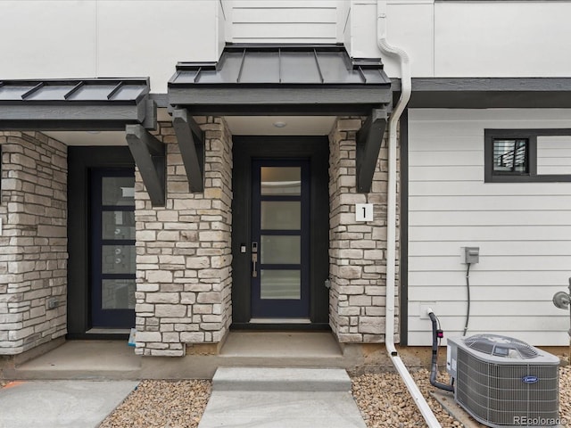 property entrance with stone siding, a standing seam roof, metal roof, and central AC unit